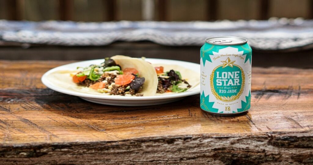 A plate of beef tacos on flour tortillas next to a cold Lone Star Rio Jade beer placed on top of a rustic wood outdoor table