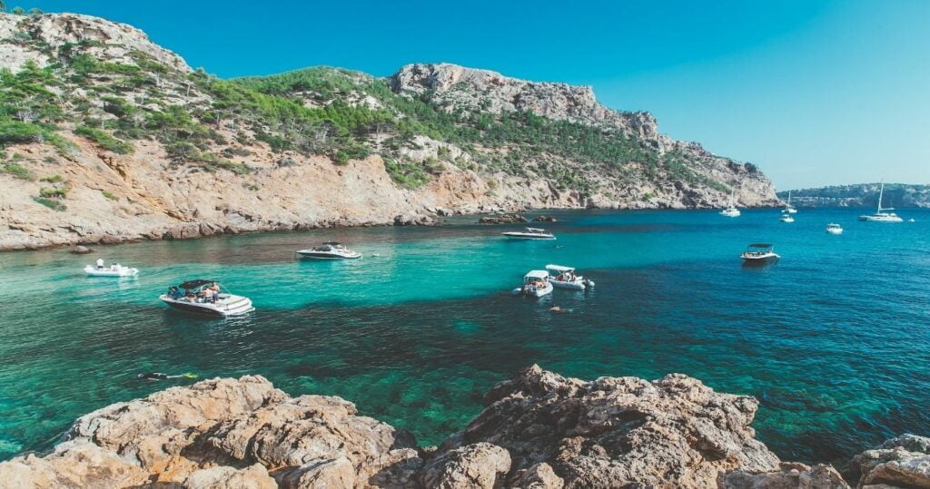 The azure blue sea dotted with boats surrounded by rocky landscapes in Palma De Mallorca, the Balearic Islands