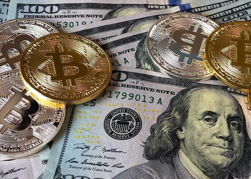 A close-up photo depicting Bitcoin coins on top of US dollar bills, symbolizing finance and cryptocurrency.