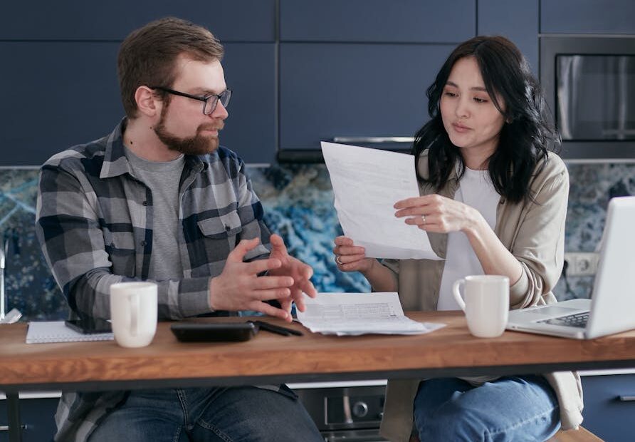 Young couple managing their finances with laptop and documents in a modern kitchen setting.