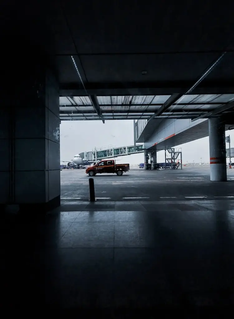 A red pickup truck parked at the terminal entrance of Kolkata Airport, with a clear view of an airplane.