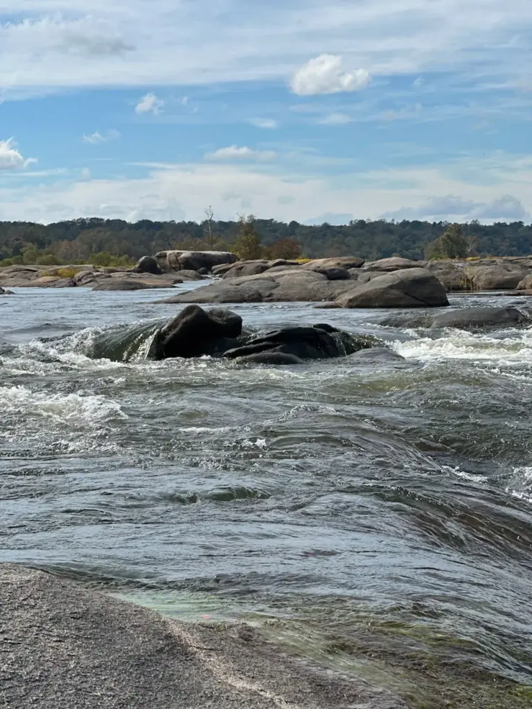 Dynamic river rapids flowing over rocks under a bright blue sky, showcasing nature's raw power.