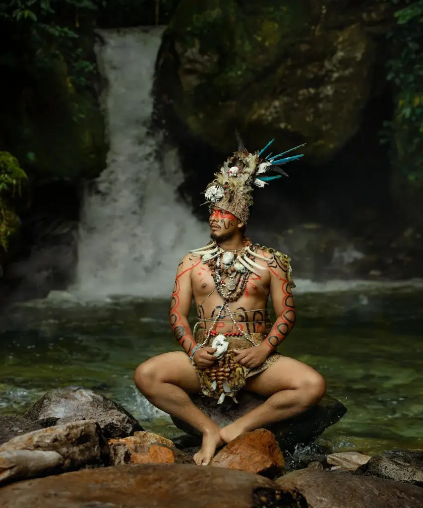 A man in traditional Peruvian attire sits by a waterfall in Tingo María, Peru.