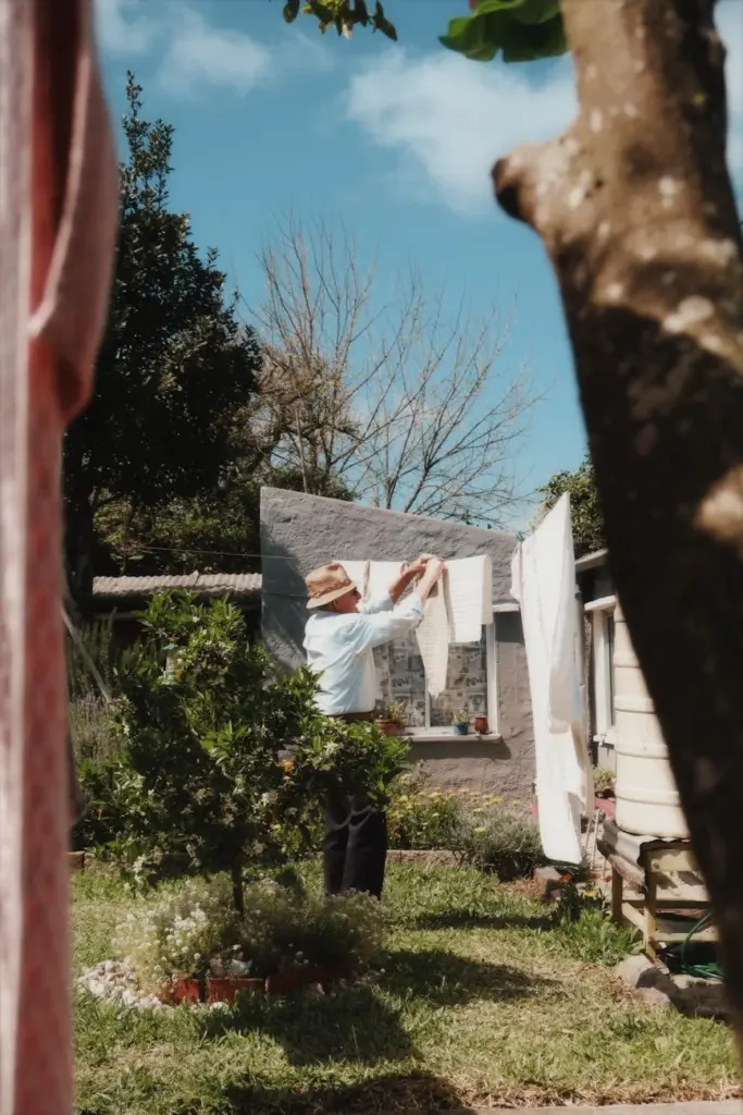 Elderly man hanging laundry outdoors in sunny garden in Melo, Uruguay.