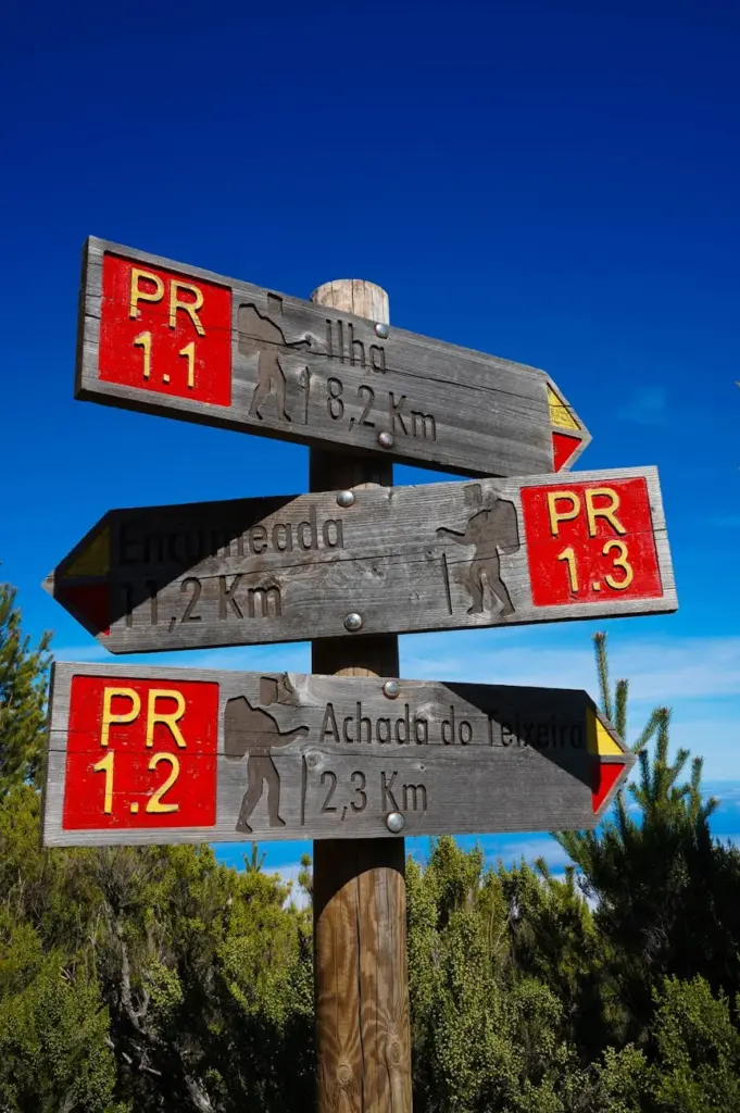 Wooden hiking trail signpost with bright red markers in a scenic outdoor setting.