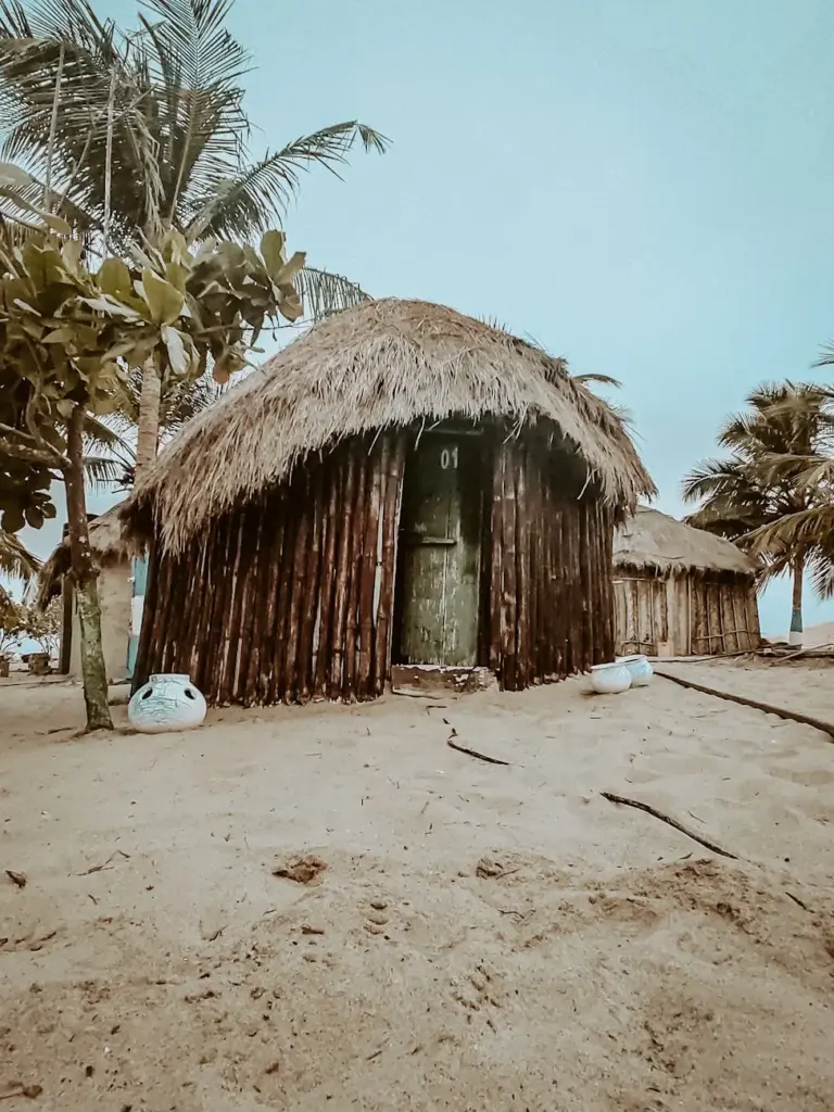 A rustic beach hut with a thatched roof nestled under palm trees on the serene coast of Keta, Ghana.