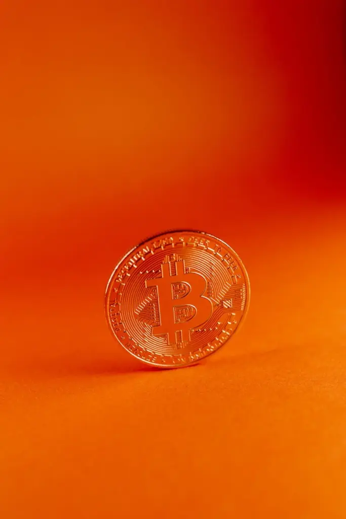 A bitcoin coin standing against a vibrant orange background, symbolizing digital currency.