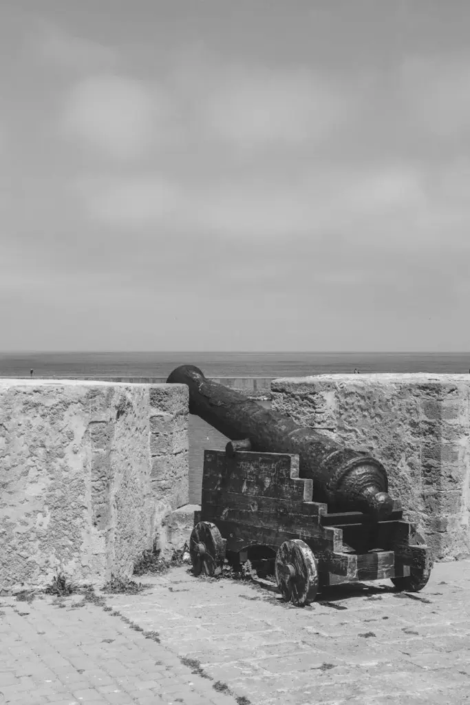 Black and white photo of an ancient cannon on El Jadida ramparts by the Atlantic Ocean, Morocco.