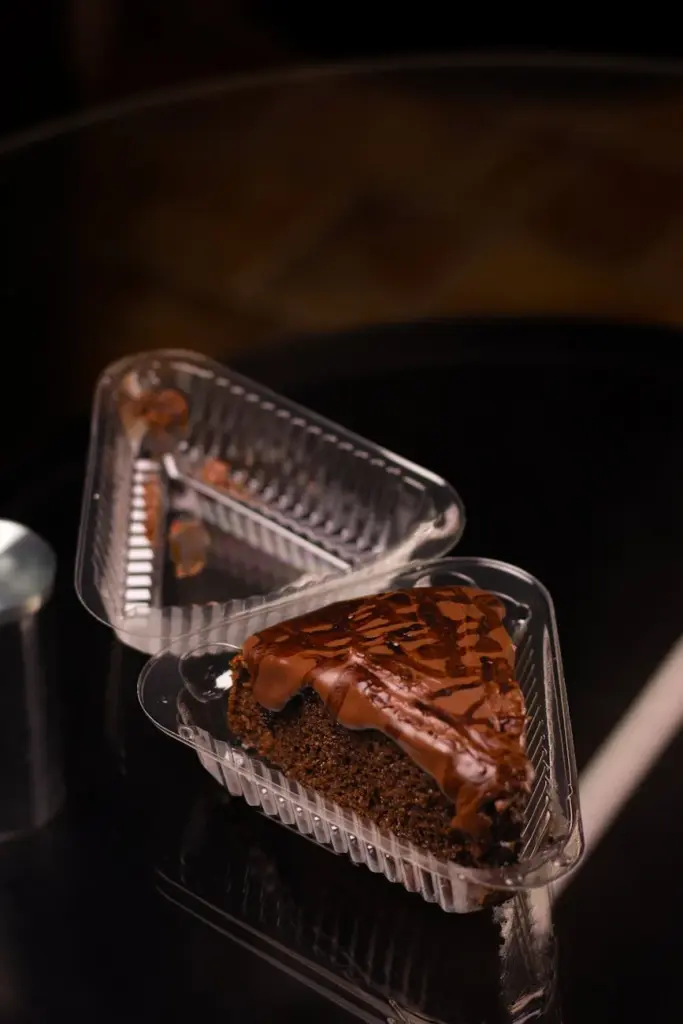 Indulgent slice of chocolate cake with drizzle captured in a plastic container on dark surface.