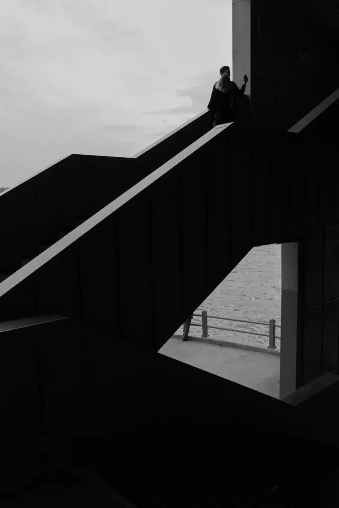 Dramatic black and white silhouette of a person on a geometric staircase by the sea.