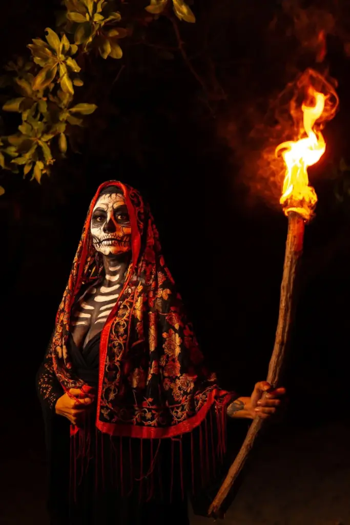 A woman in Dia de Muertos attire holds a torch, showcasing Mexican culture in Acapulco.