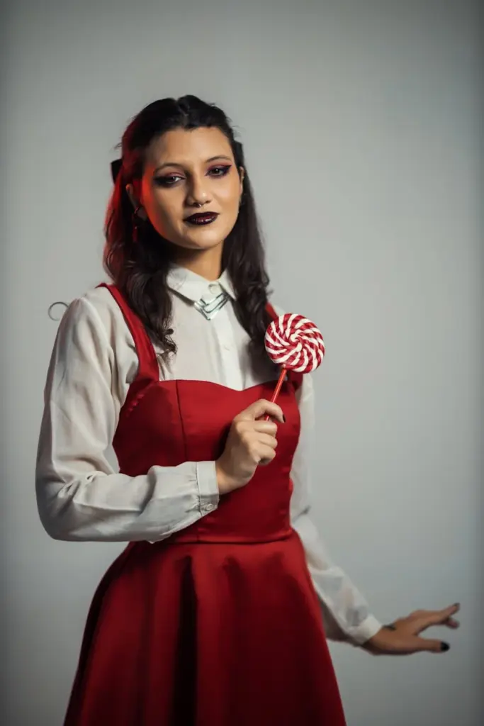 A fashionable woman in a red dress stands with a lollipop, exuding elegance and charm.
