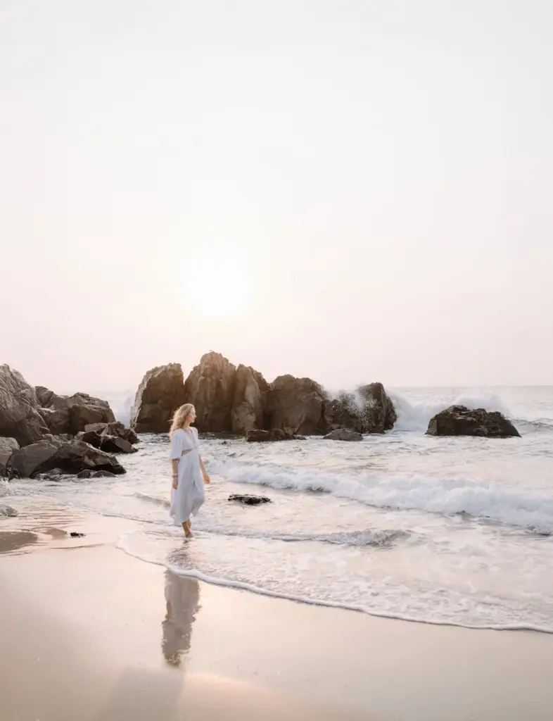 A serene scene of a woman walking along a rocky beach at sunrise.