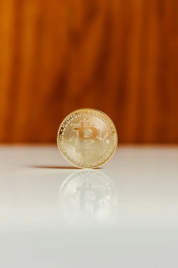 Golden Bitcoin standing upright on a shiny white surface against a wooden background.