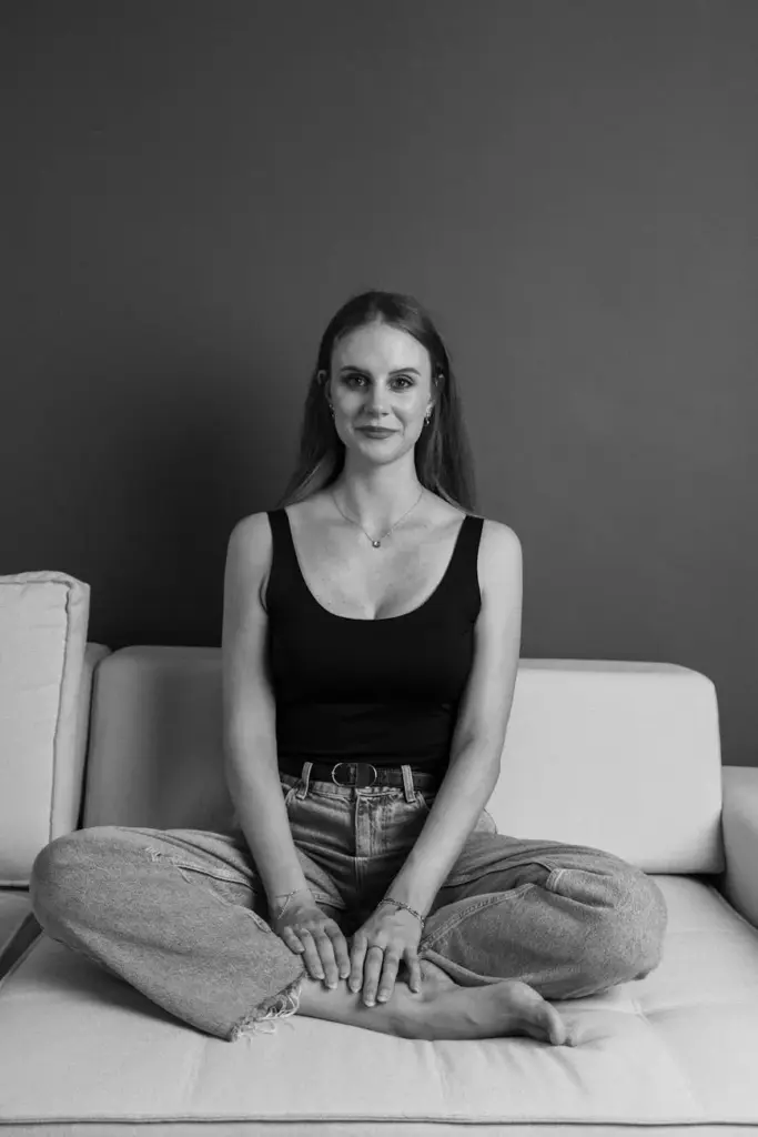 A woman in casual attire sitting cross-legged on a sofa, captured in monochrome.