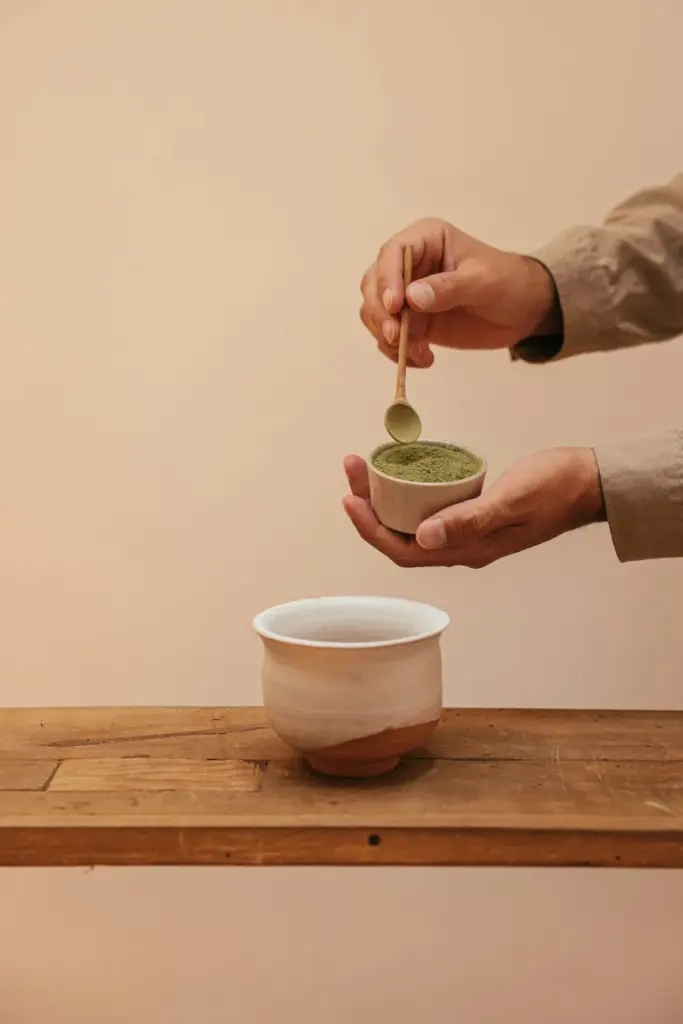 Hands preparing matcha tea with a wooden spoon during a tea ceremony.