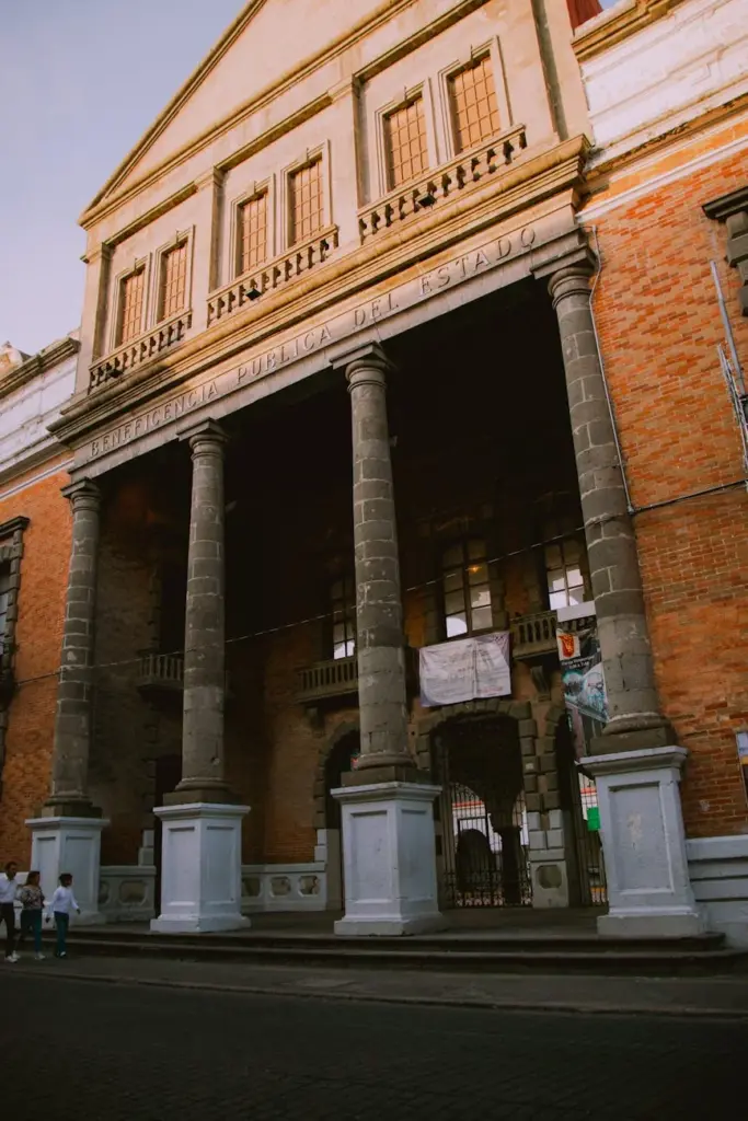 Exterior view of a historic Mexican library with stone columns and red brick facade.