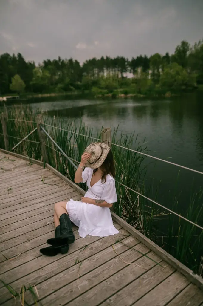 Woman in white dress sitting on a bridge by the lake, enjoying a serene summer day.