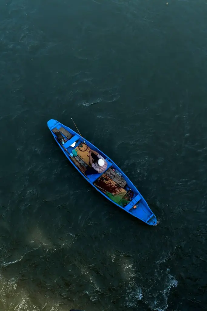Aerial shot of a fisherman sitting in a blue boat on expansive water, casting a tranquil fishing scene.