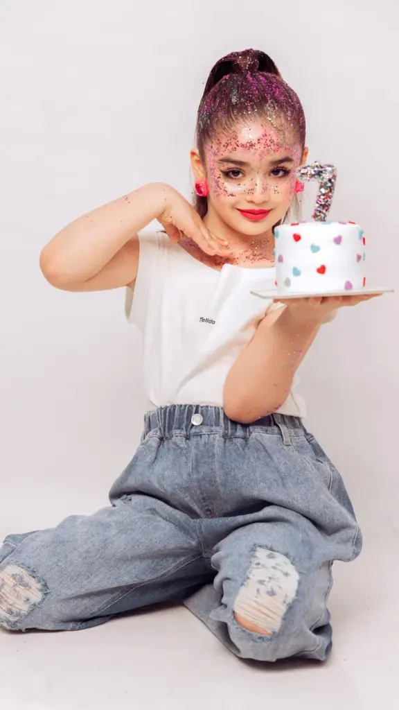 Child in sparkly outfit presenting a heart-patterned cake, ideal for birthday themes.