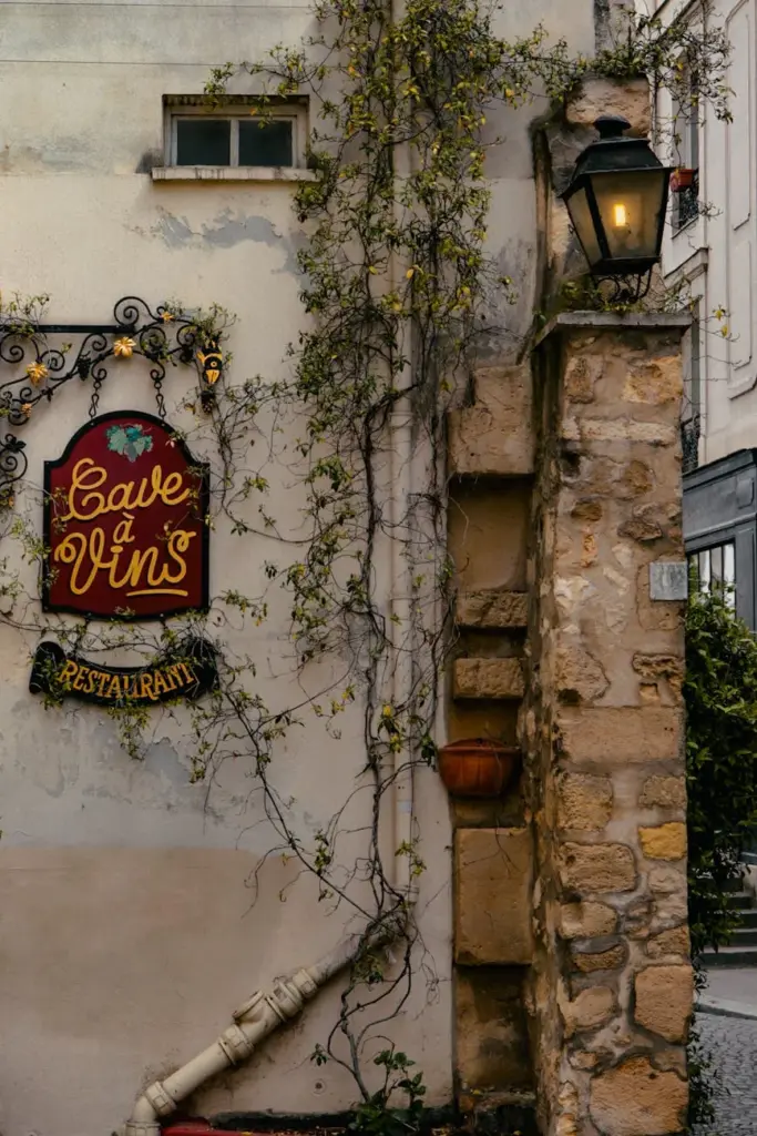 Rustic outdoor view of a Paris wine cellar with climbing vine and vintage sign.