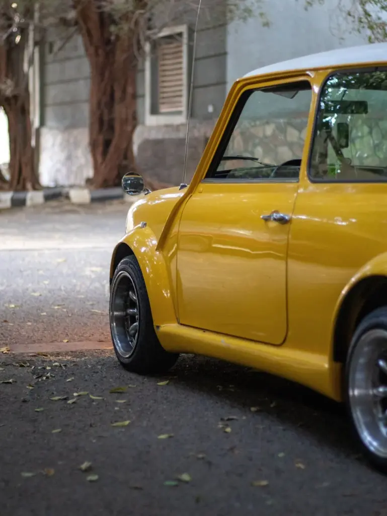Side view of a vintage yellow Mini car parked outdoors, showcasing its classic design.