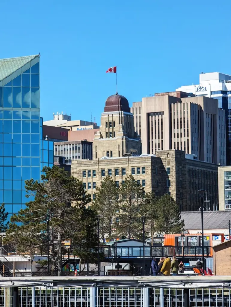 Vertical shot of the Dominion Public Building against Halifax's cityscape with trees in the foreground.