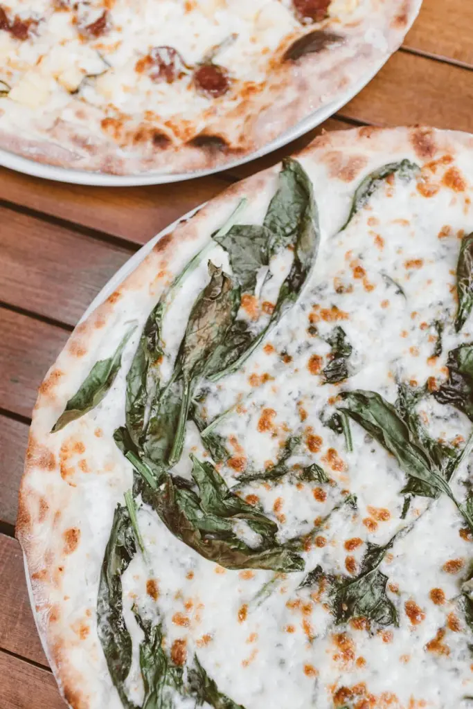 Top view of artisanal pizzas on wooden table, showcasing fresh ingredients and melted cheese.
