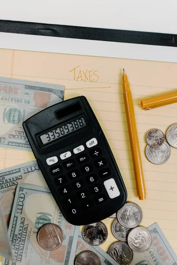 A financial planning setup with calculator, cash, and coins on a notepad labeled 'Taxes.'