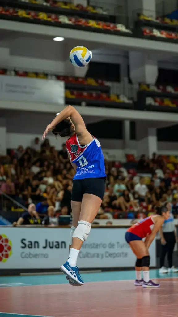 Dynamic action shot of a female volleyball player in mid-air during a serve in a professional match.