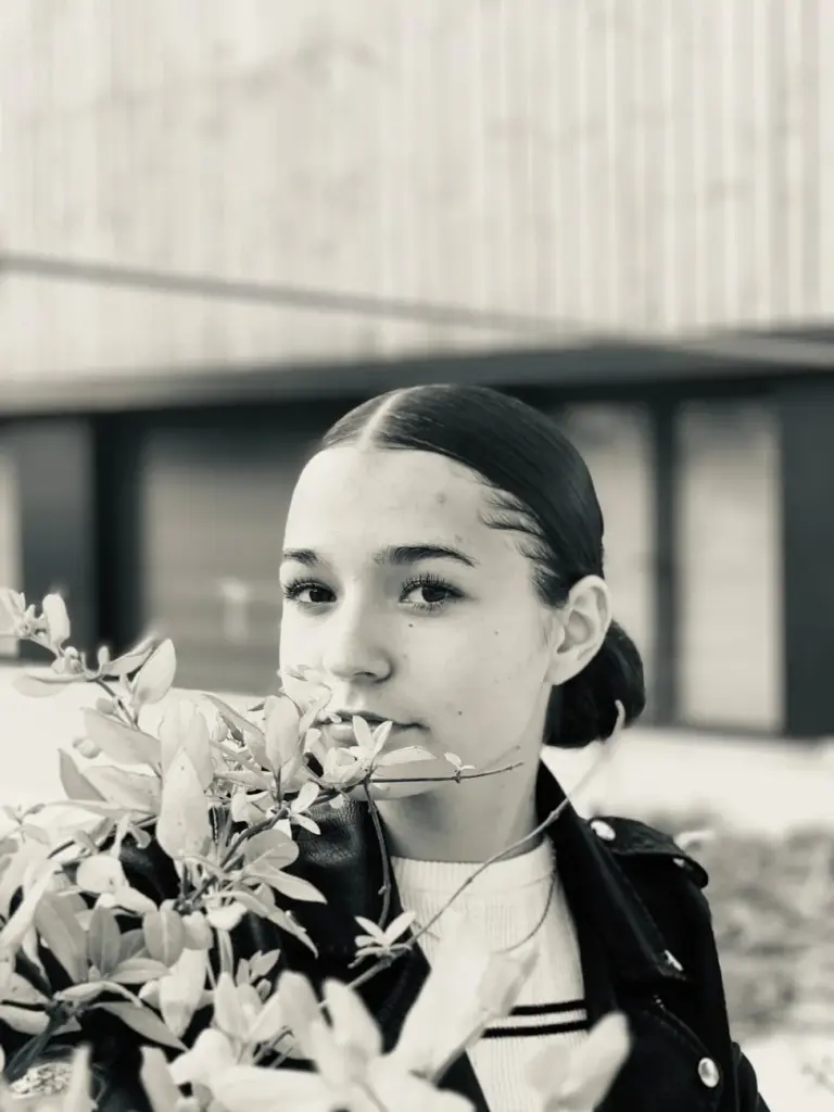 Black and white portrait of a young woman holding leaves, exuding natural elegance.