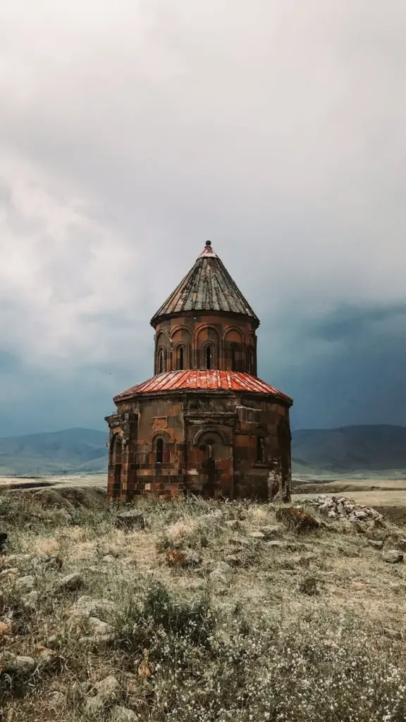 Aged round stone church standing alone on a rural hillside under an overcast sky.