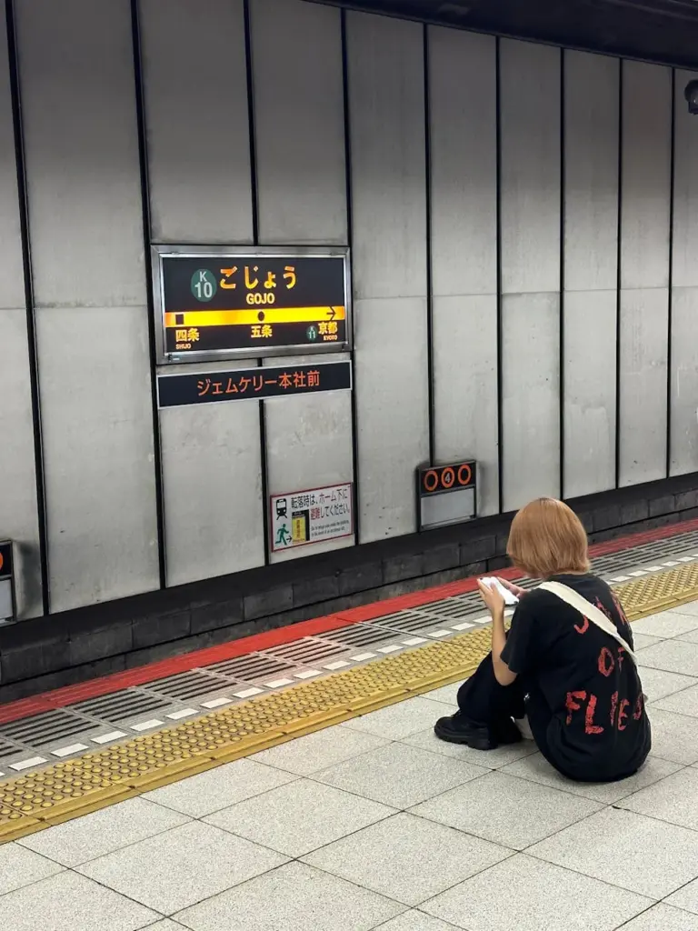 A woman sitting at Gojo Station platform in Kyoto, Japan, reading her phone.