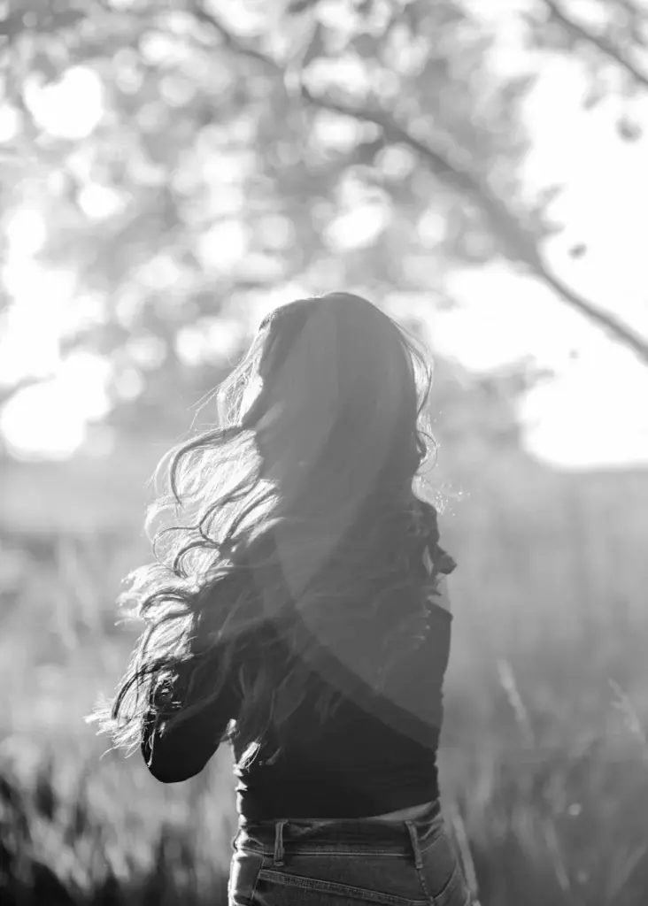 Elegant black and white portrait of a woman in nature with sunlit hair.