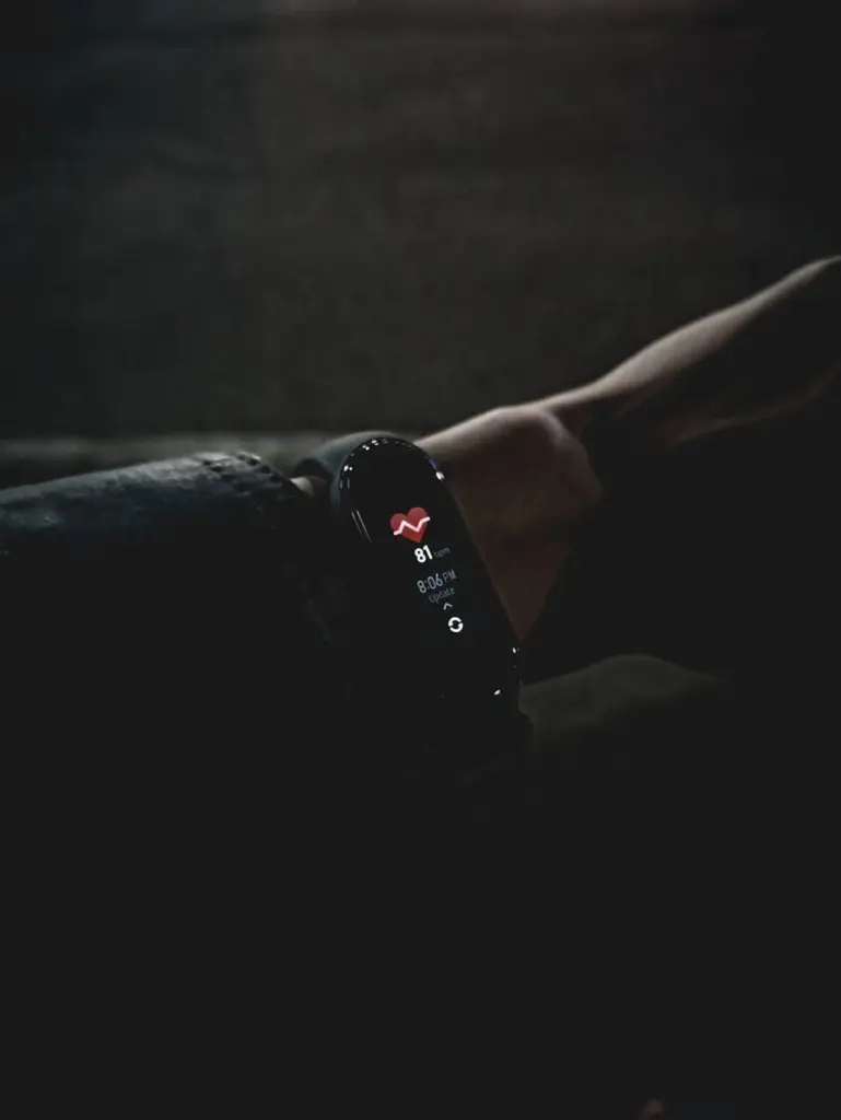 A close-up image of a fitness tracker displaying vital signs on a person's wrist in low light conditions.
