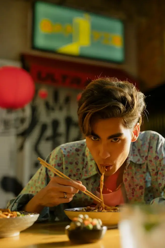 Man savoring noodles using chopsticks in a traditional Asian restaurant setting.