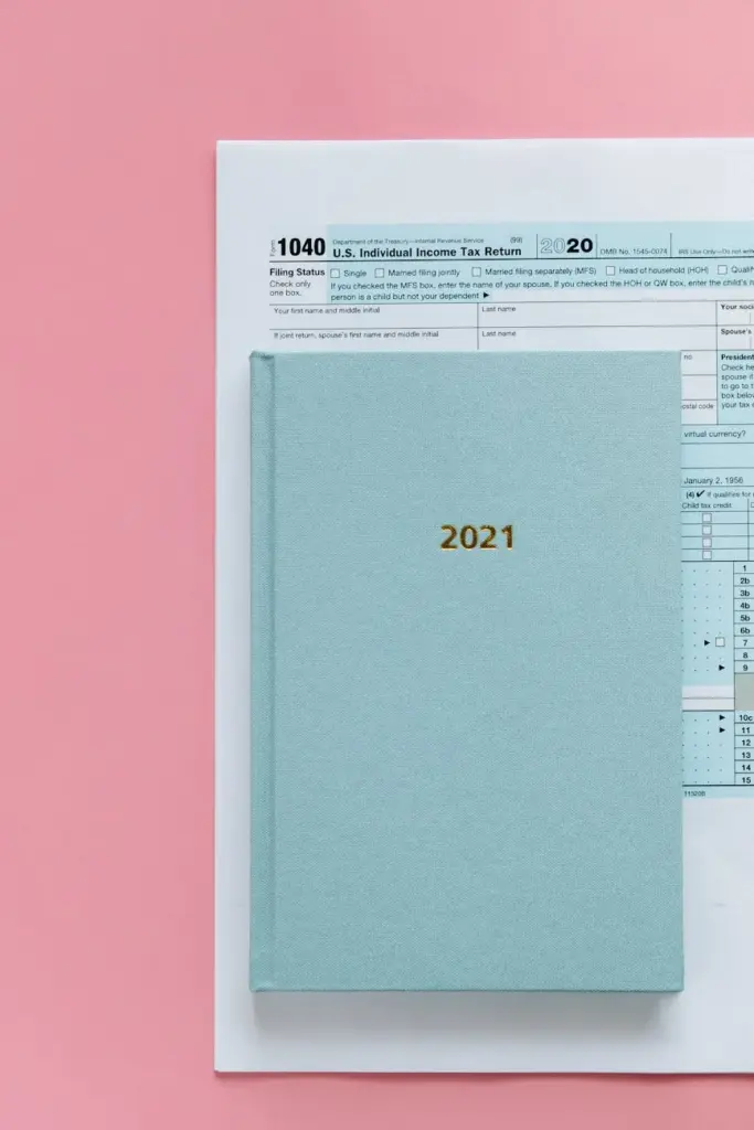 Flat lay of a 1040 tax return form and a 2021 planner on a pastel pink background.