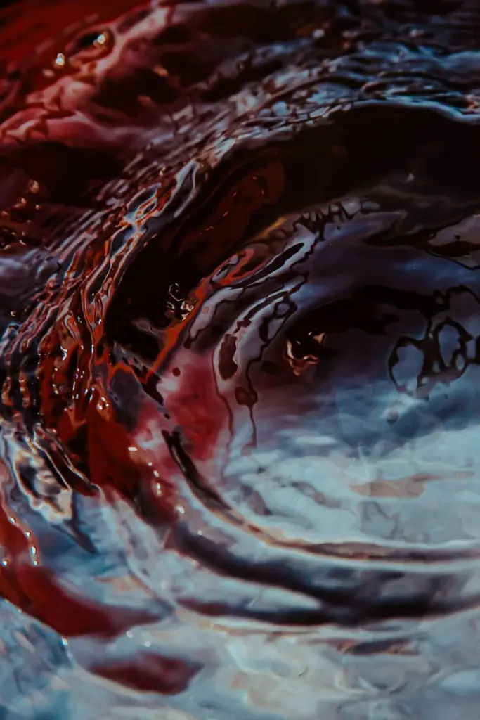 Captivating close-up of ripples forming on a liquid surface, featuring rich red and blue shades.