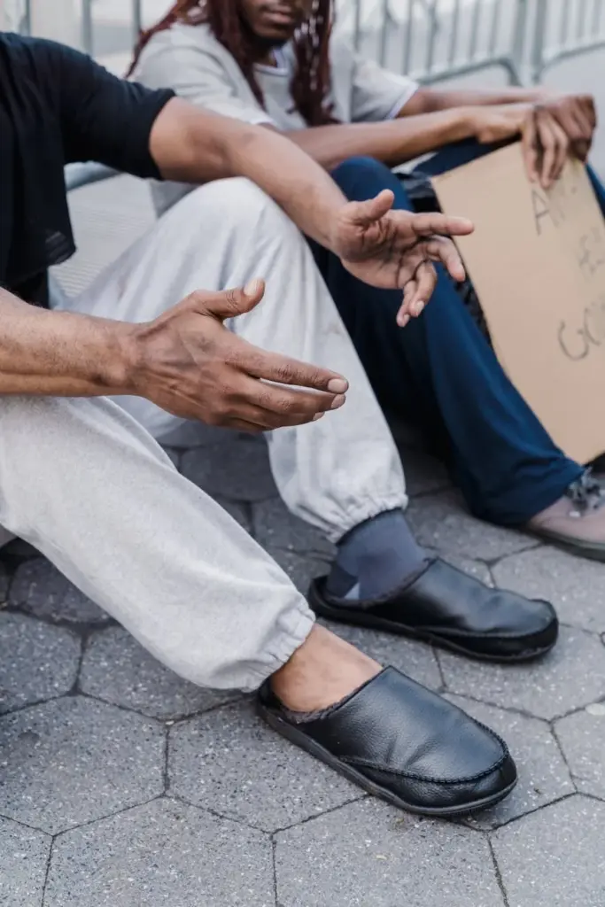 Two men sitting on a city street, holding a cardboard sign, emphasizing urban poverty.