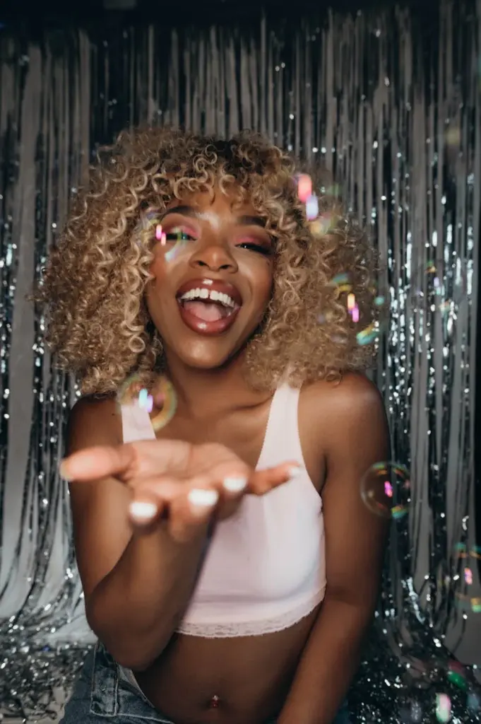A woman with curly hair enjoys a festive celebration with bubbles indoors.