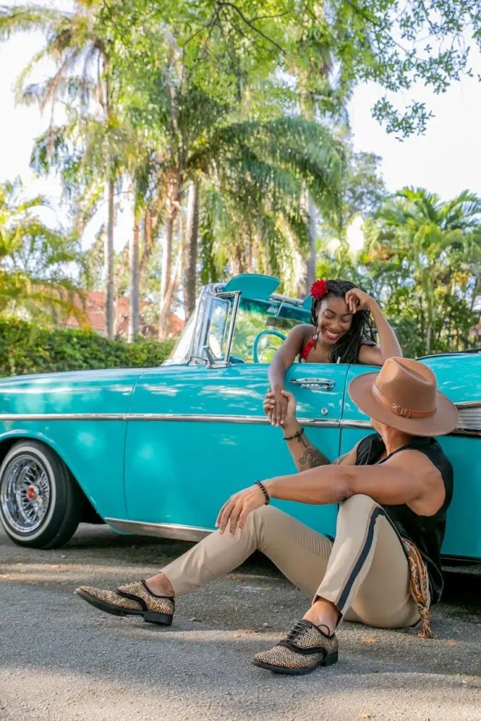 Couple enjoying a moment by a classic vintage car in a tropical setting with palm trees.