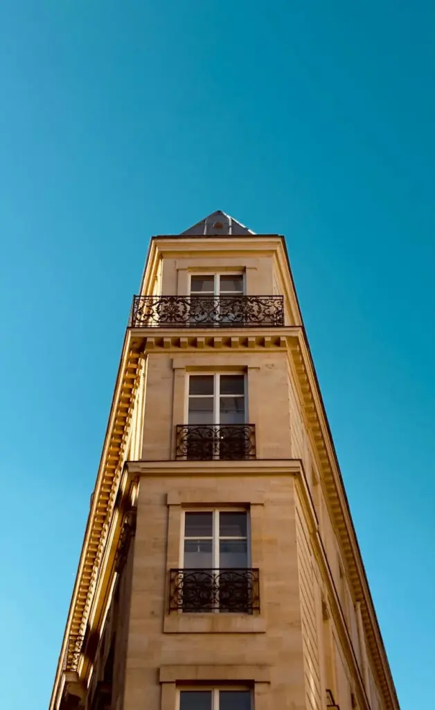 Classic Parisian Haussmann building with iron balconies under a summer sky.
