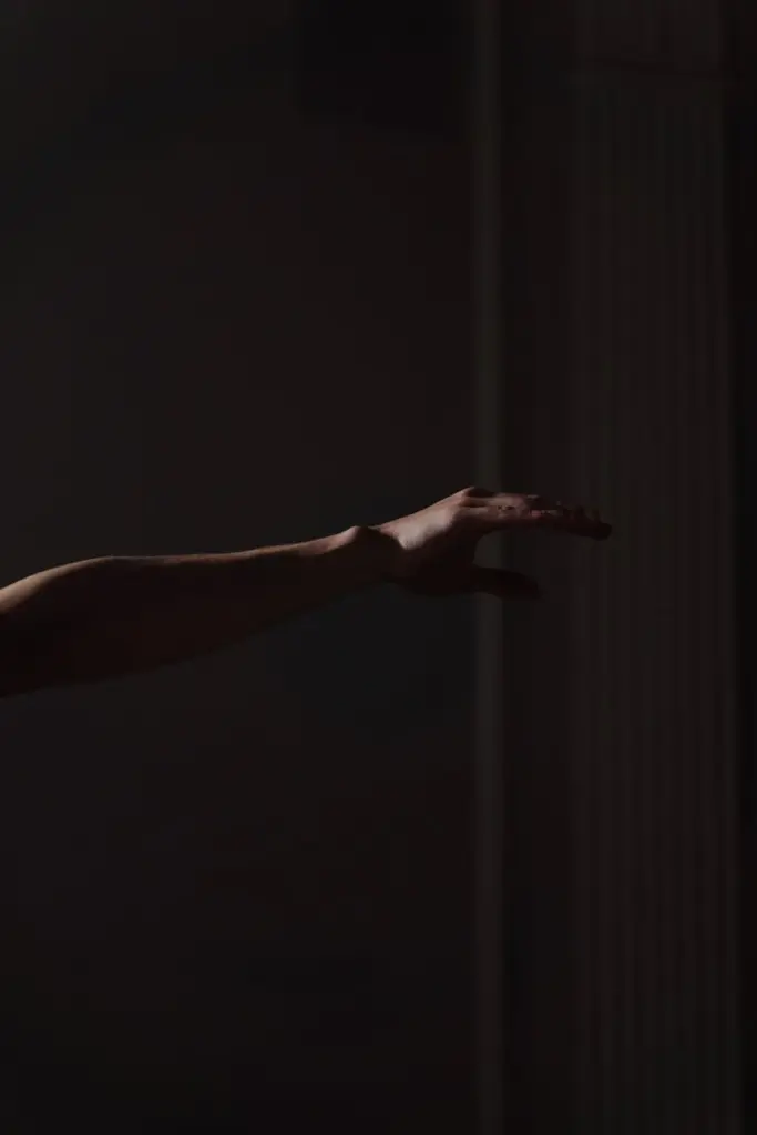 A shadowed arm extended in a dark, minimalist setting.