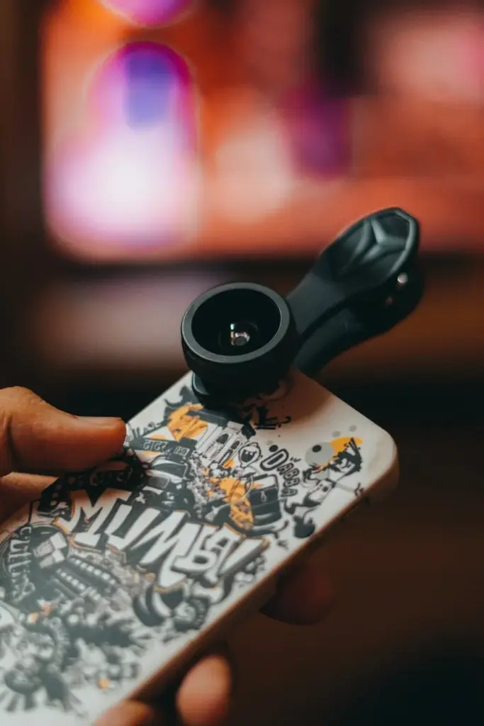Smartphone with clip-on lens held in hand, capturing close-up shots indoors.