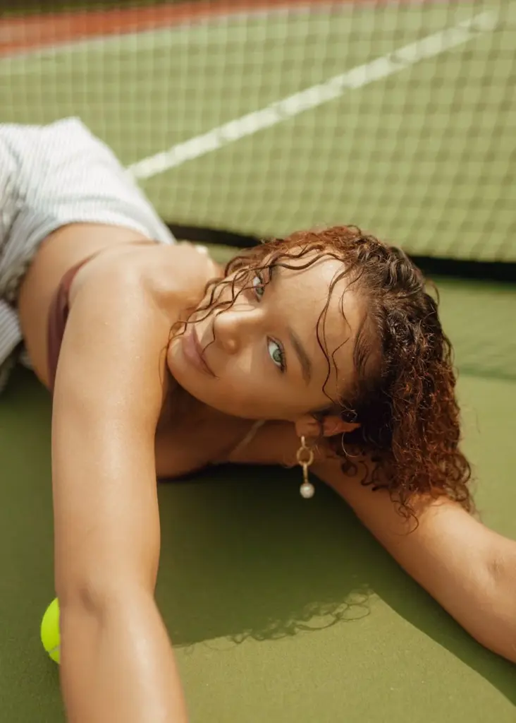 A beautiful woman lying down on a tennis court, conveying relaxation and style.
