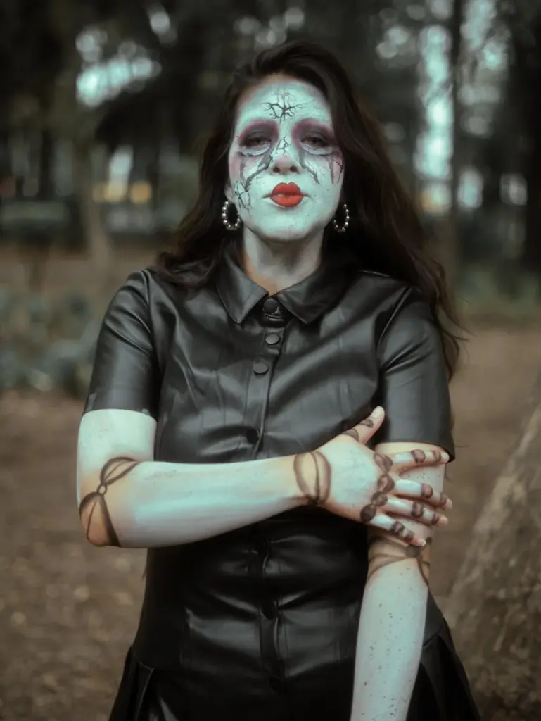A haunting image of a woman styled as a creepy doll with cracked face paint, outdoors.