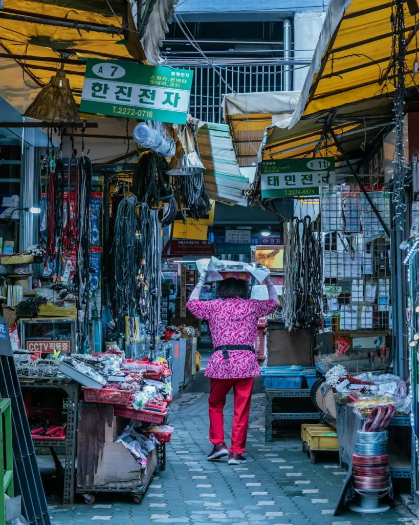 Vibrant scene of a merchant carrying goods in a bustling Seoul market alleyway.