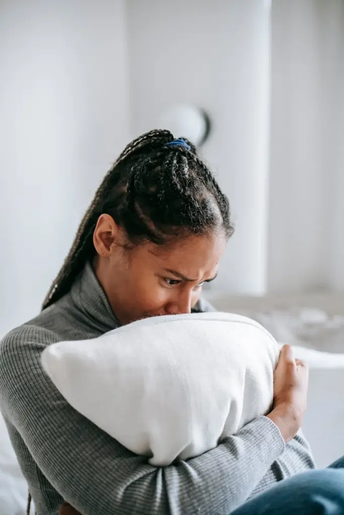 Pensive woman sitting indoors, clutching a pillow with a worried expression.