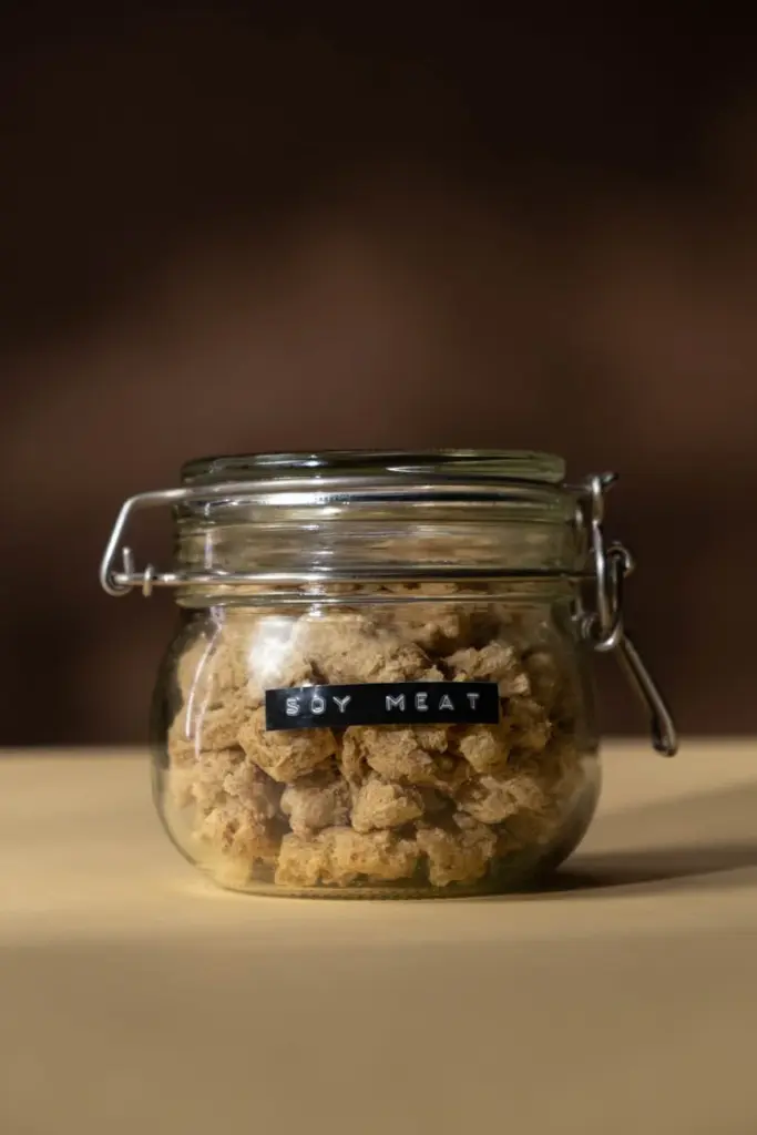 Close-up of glass jar containing dry soy meat chunks, emphasizing healthy and vegan alternative.