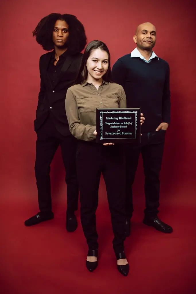Diverse business team holding an award on a red background showcasing achievement.